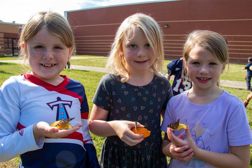 Three girls smile while holding butterflies